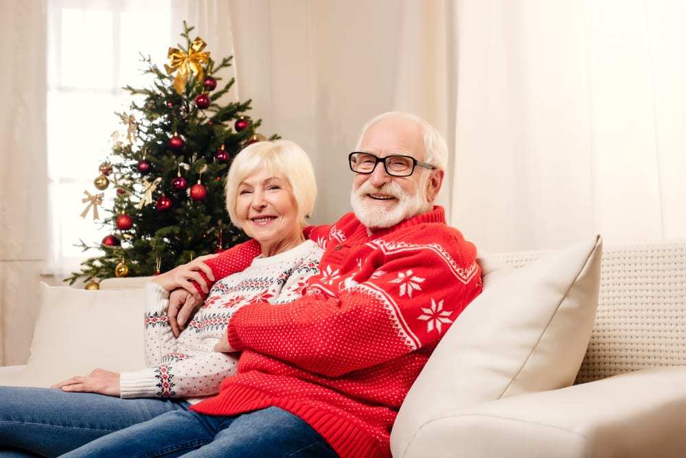 senior couple wearing christmas sweaters smiling on couch
