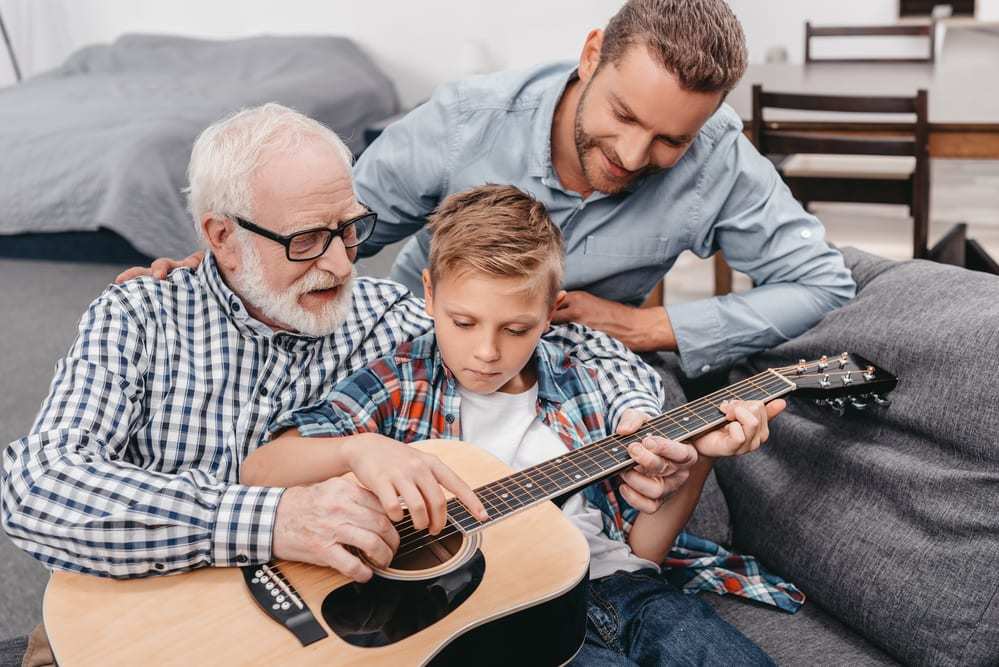 Senior man teaching grandson to play guitar, son looking over them