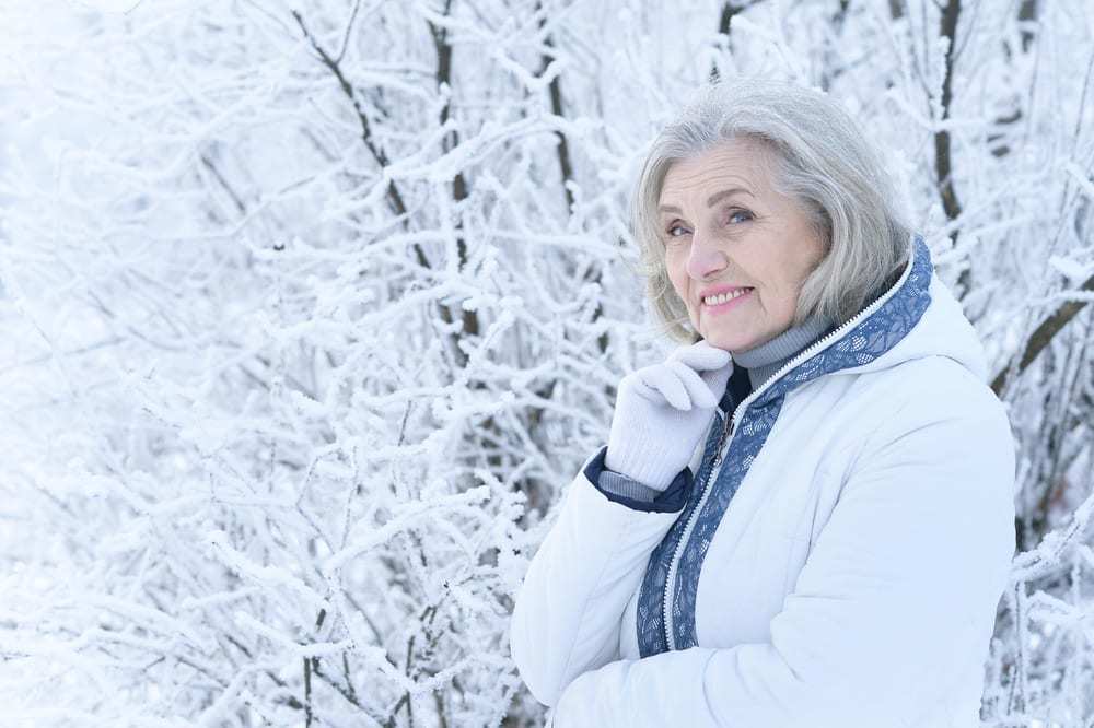senior woman with thoughtful expression, outside in snowy wooded environment