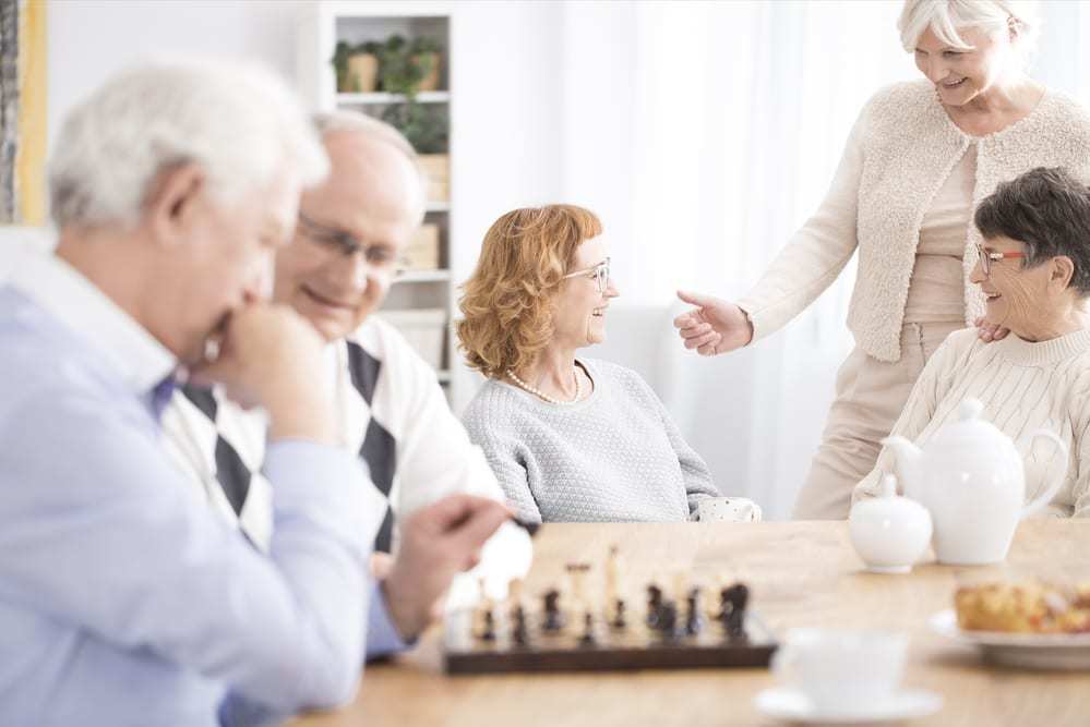 A group of seniors spending time together talking and playing chess