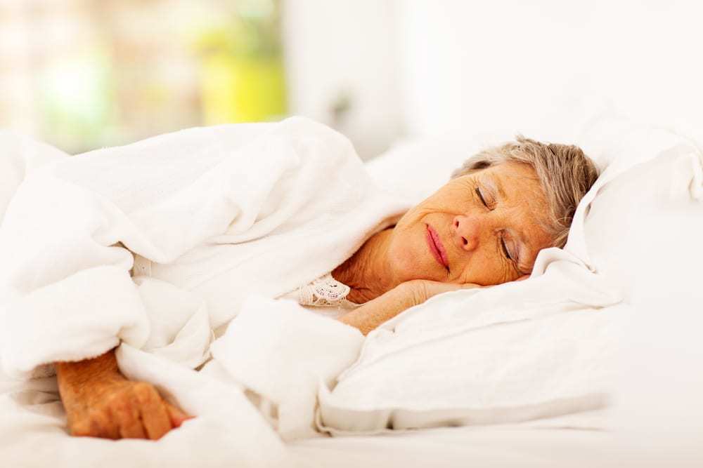 Senior-woman-asleep-on-her-side-in-bed-bright-morning-light