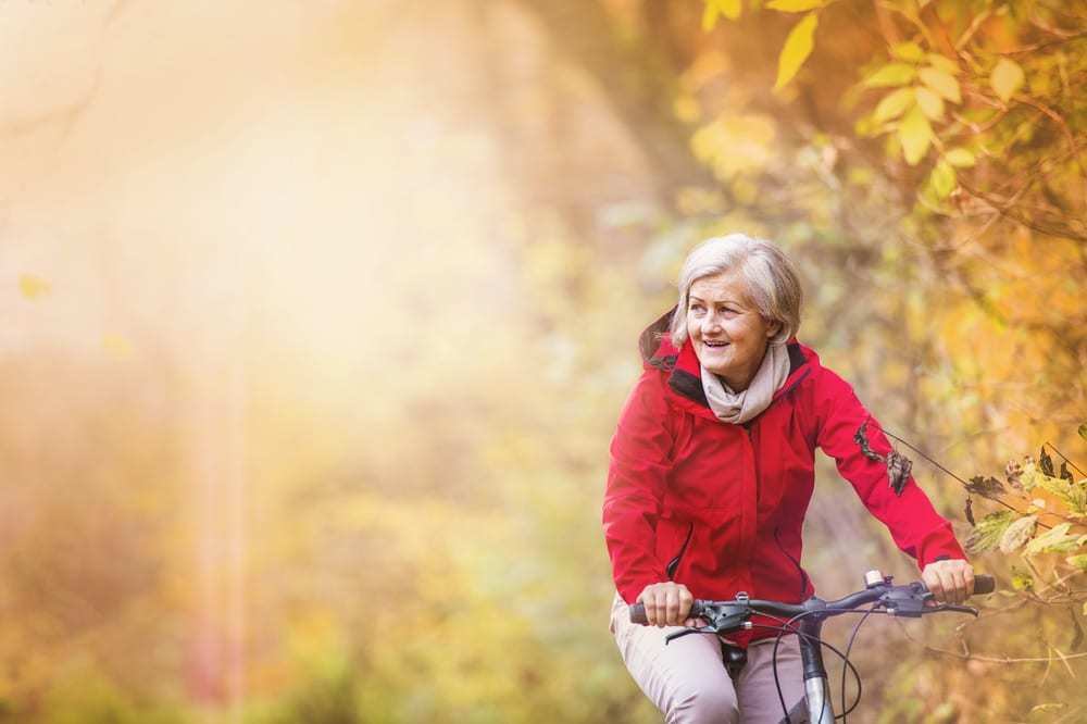 Senior-woman-riding-on-bike-autumn-leaves-in-background
