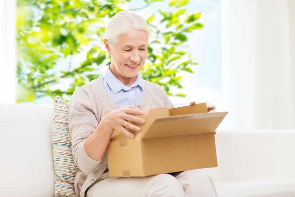 Smiling-senior-woman-opening-cardboard-package-at-home