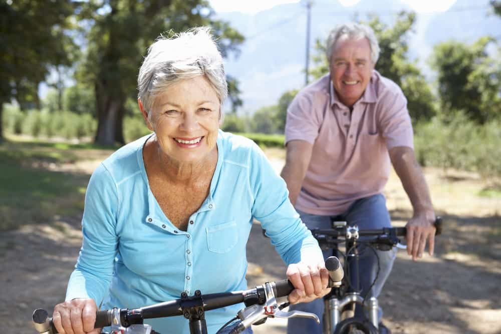 Two-smiling-seniors-bicycling-outside