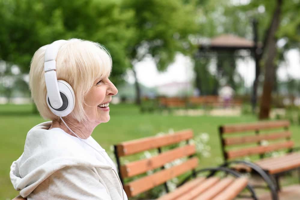 smiling-senior-woman-wearing-headphones-in-park