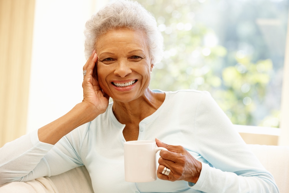 Senior woman smiling and holding mug while sitting on couch