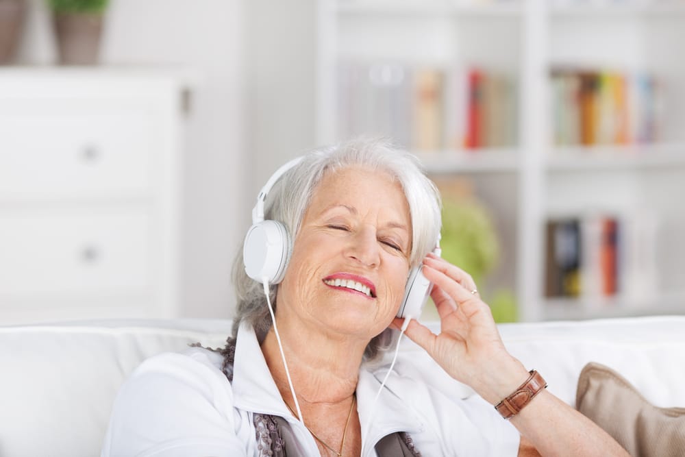 Smiling senior woman listening to music using headphones at home