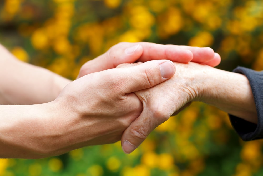 Younger hands holding older hands outdoors in autumn