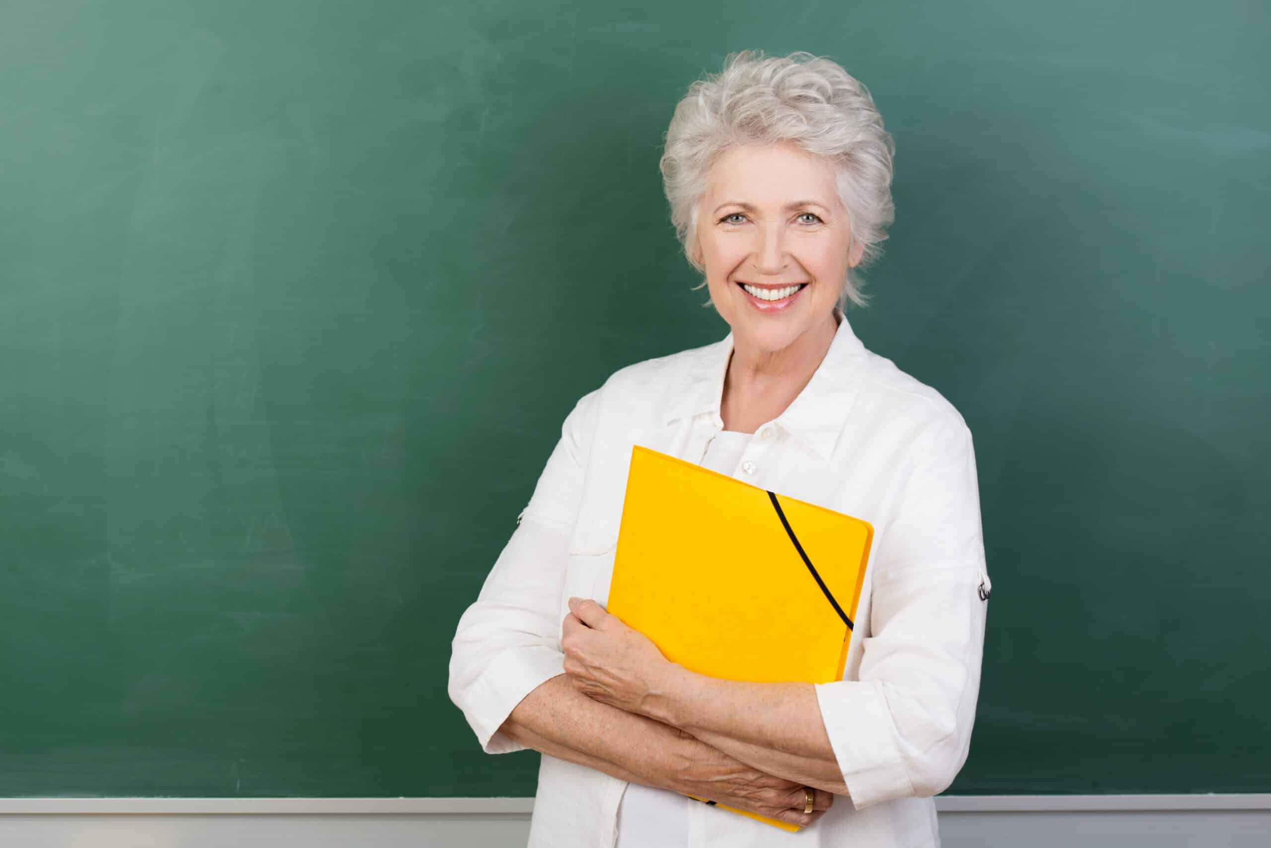 Smiling senior woman holding notebook or folder in front of chalkboard