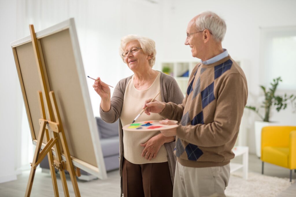 Two seniors smiling and painting on canvases