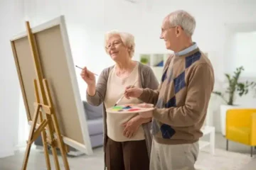 two seniors smiling and painting on canvas