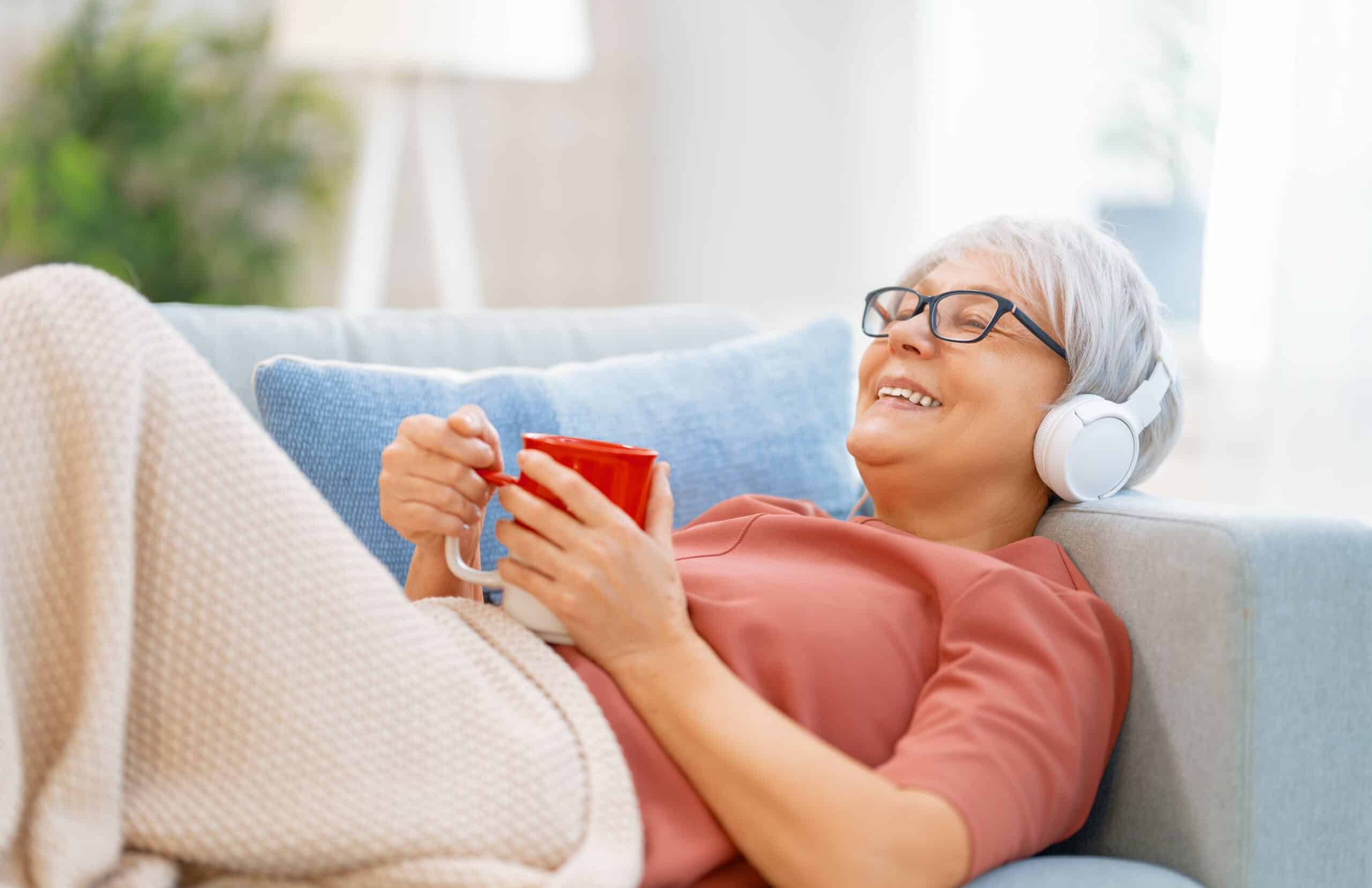Senior woman listening to audiobook on couch, relaxed
